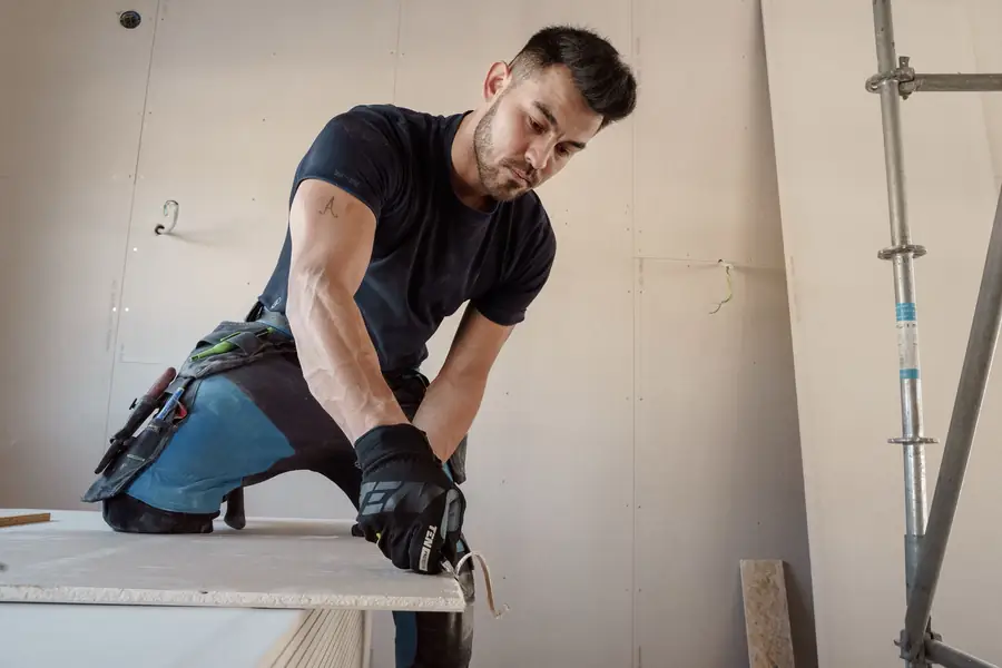 Plaquiste découpant une plaque de plâtre sur un chantier